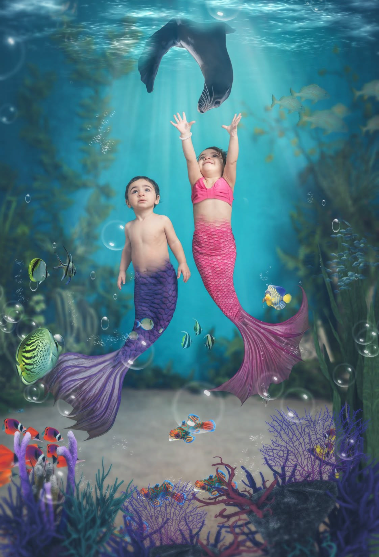 A young girl dressed as a mermaid with purple tail poses underwater surrounded by colorful fish, seaweed, and bubbles.