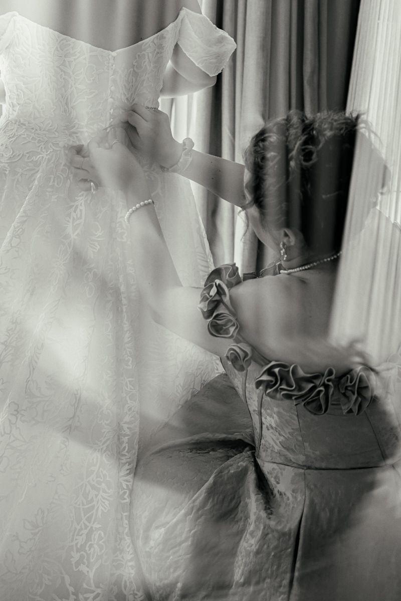 Black and white double exposure photo of a bride in a lace wedding dress and veil near a window.
