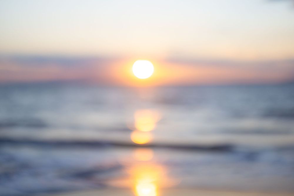 Blurred bokeh sunset over calm ocean waves with warm golden and pink hues reflecting on the water.