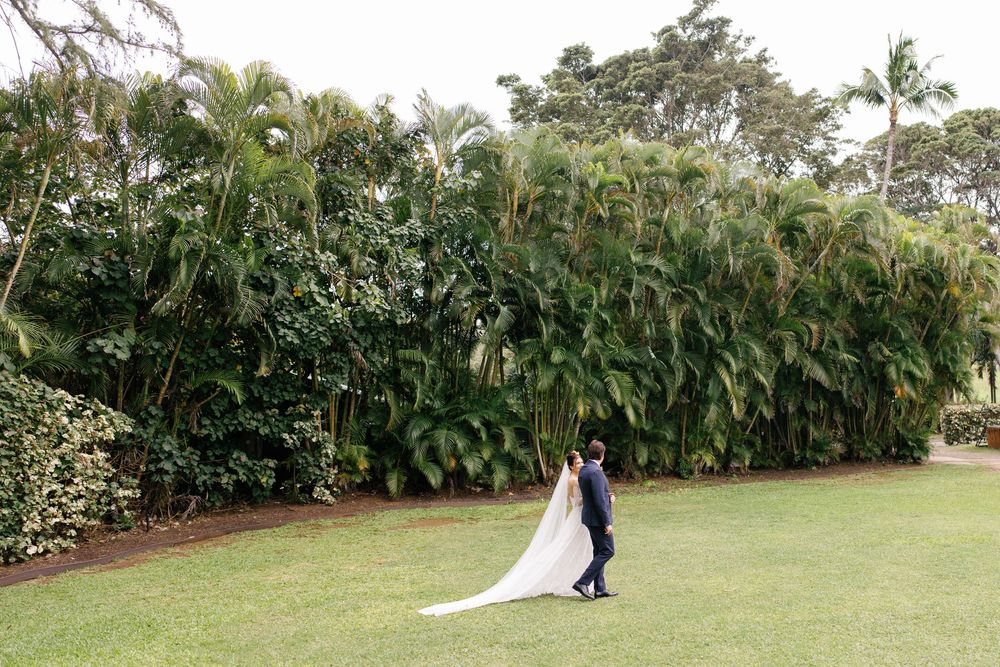 Bride and groom walking on lush green lawn with tropical palm trees backdrop at outdoor wedding ceremony.
