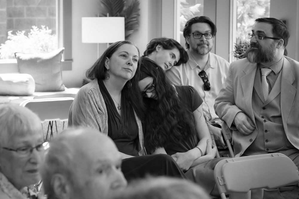 Black and white photo of guests seated at an indoor gathering, socializing and relaxing in a bright room.
