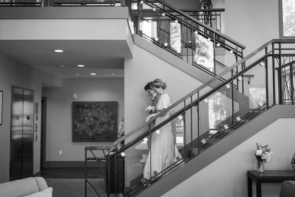 Bride in white gown descending elegant staircase in black and white wedding photo.