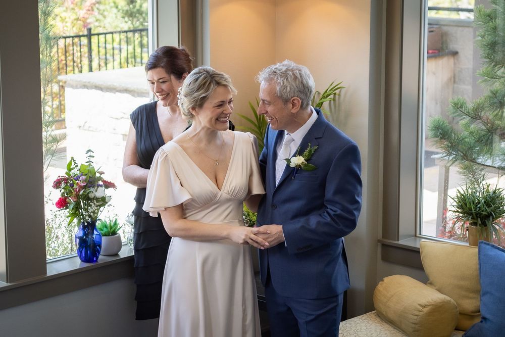 Bride and groom share a joyful moment with officiant during intimate indoor wedding ceremony.