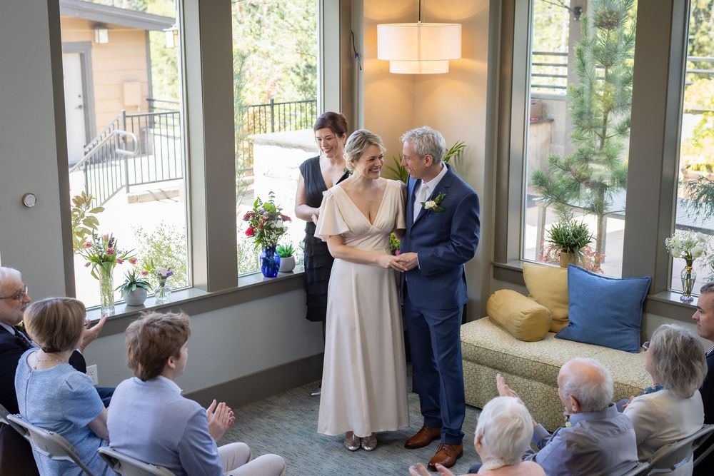 Couple exchanging vows in bright sunlit room with small intimate wedding gathering.