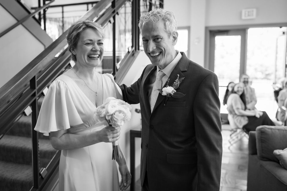 Black and white photo of a laughing bride and groom walking together at their wedding ceremony.