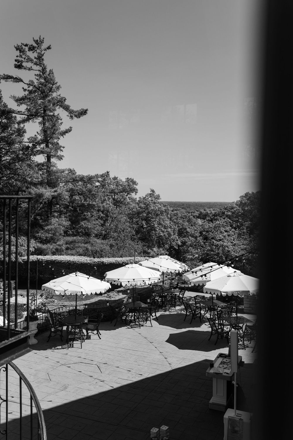 Black and white photo of an outdoor restaurant patio with umbrellas, tables, and chairs surrounded by lush trees.