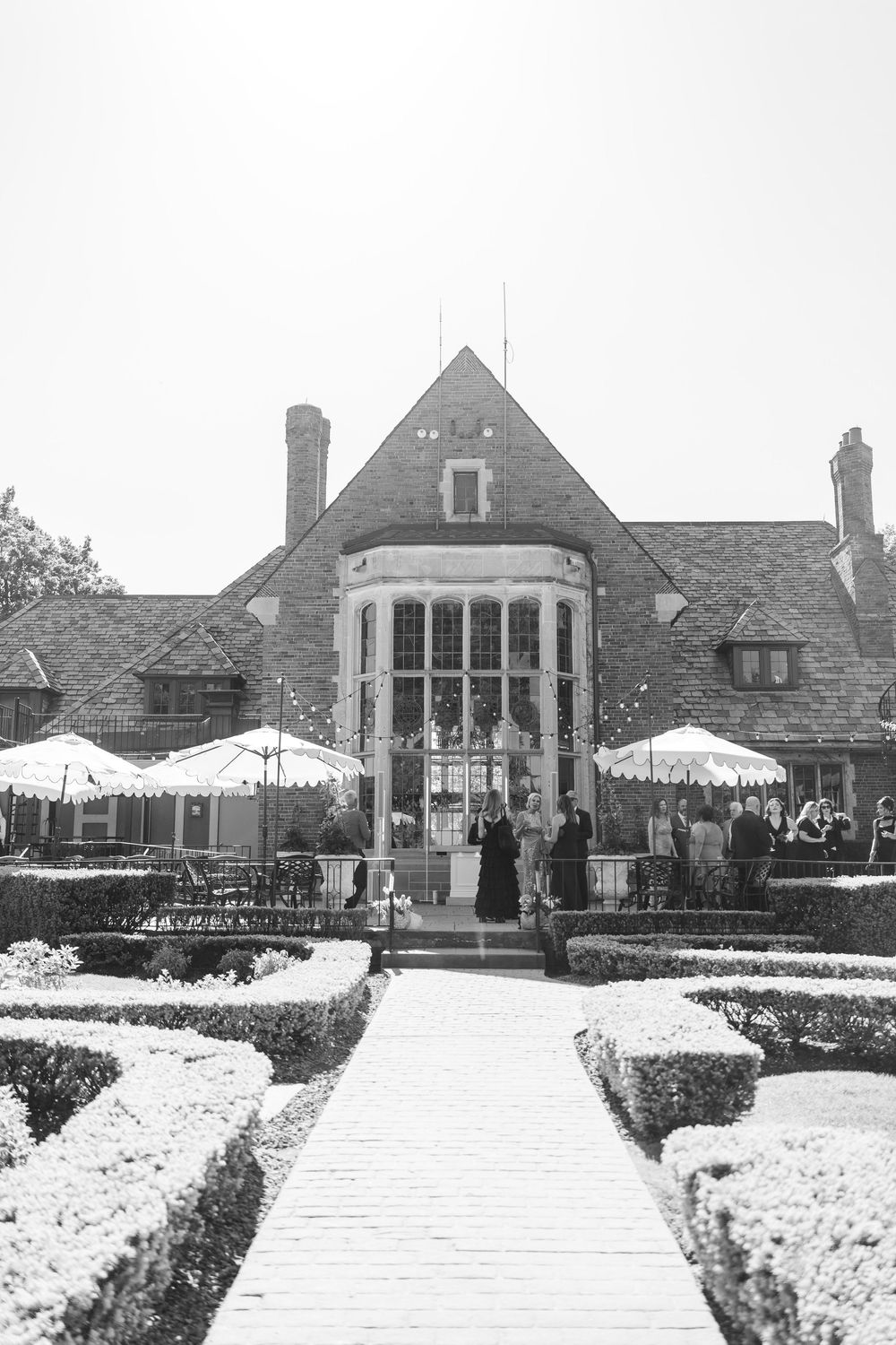 Black and white photo of elegant Tudor-style wedding venue exterior with manicured hedgerow gardens.
