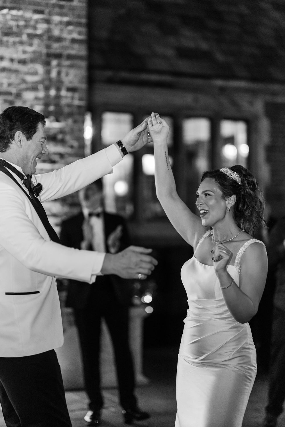 Black and white photo of groom twirling laughing bride during energetic first dance at wedding reception.