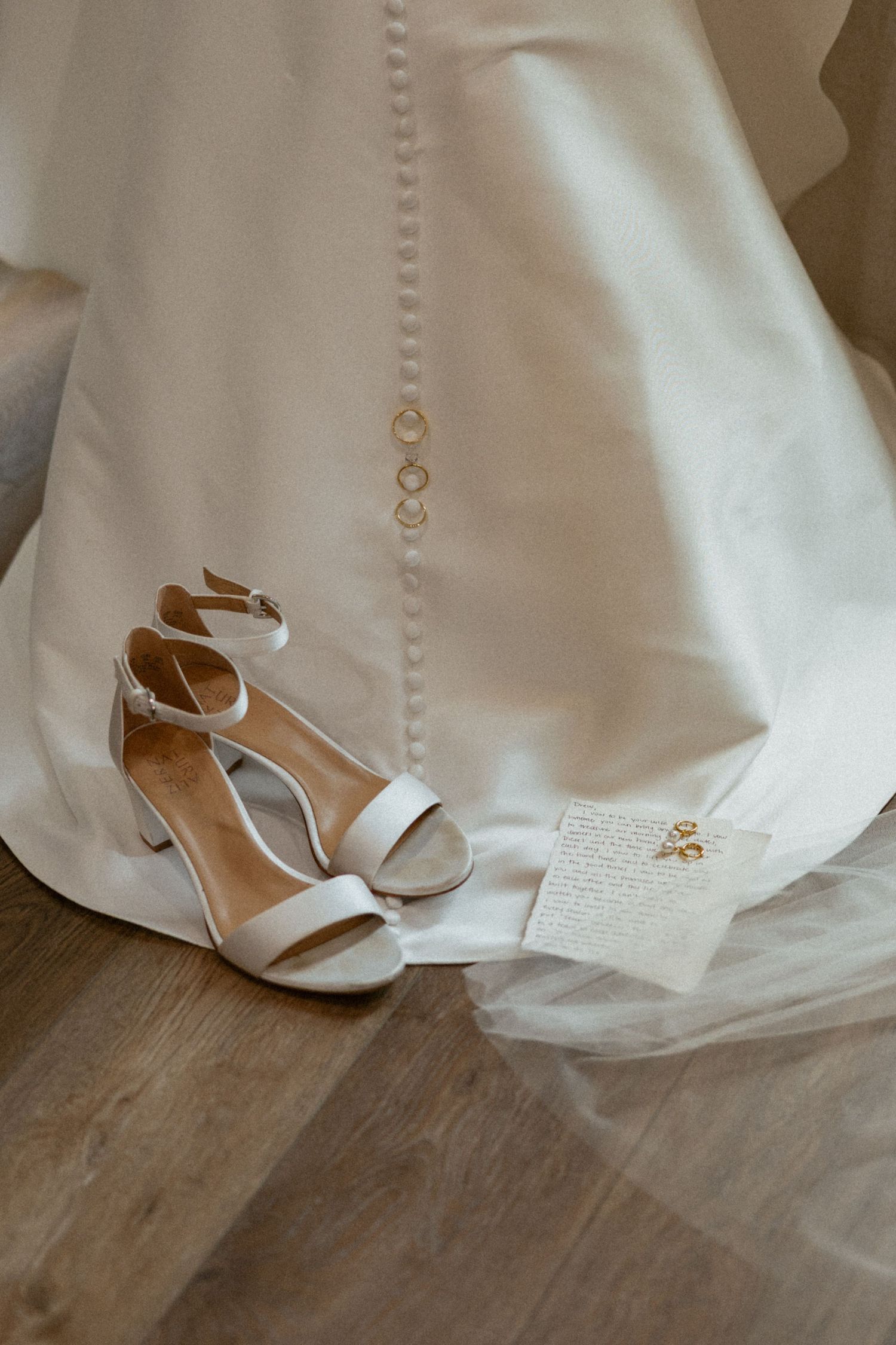 Black and white photo of two wedding rings displayed on a bridal gown with delicate button detailing.
