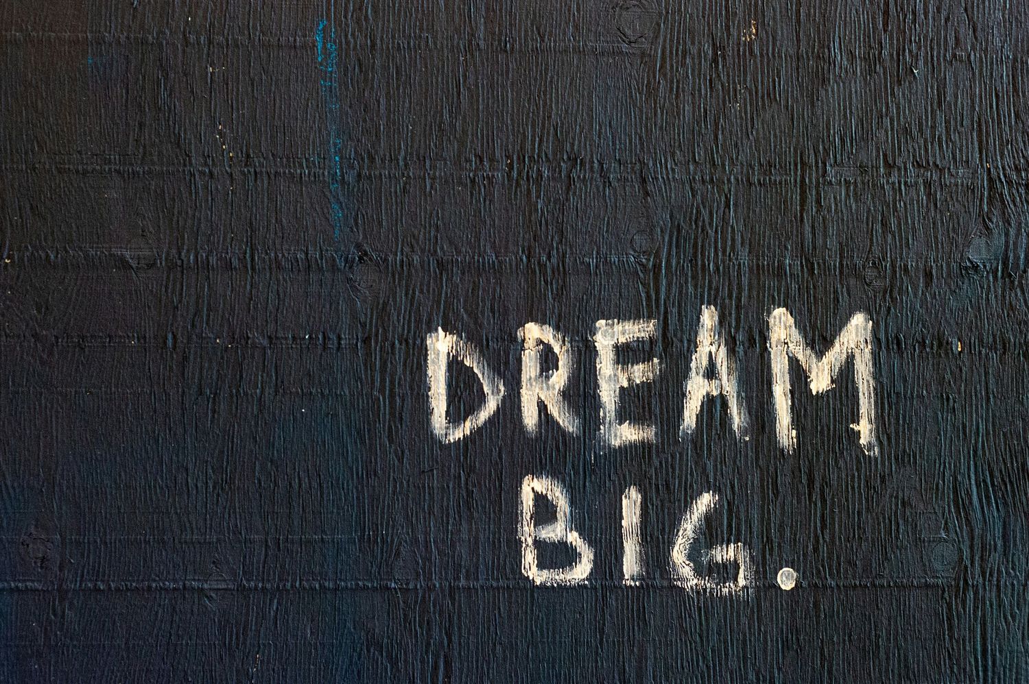 Black wall with white graffiti text reading Dream Big, inspirational street art motivational quote.