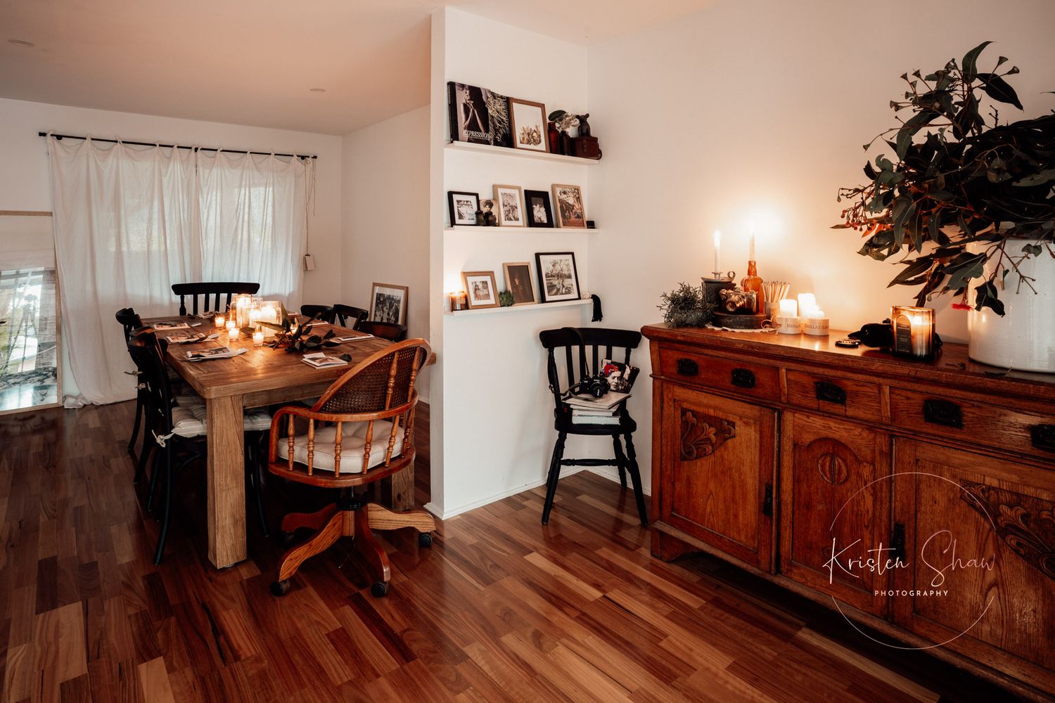 Cozy dining room with wood furniture, hardwood floors, warm candlelight, and rustic sideboard with decorative shelves.