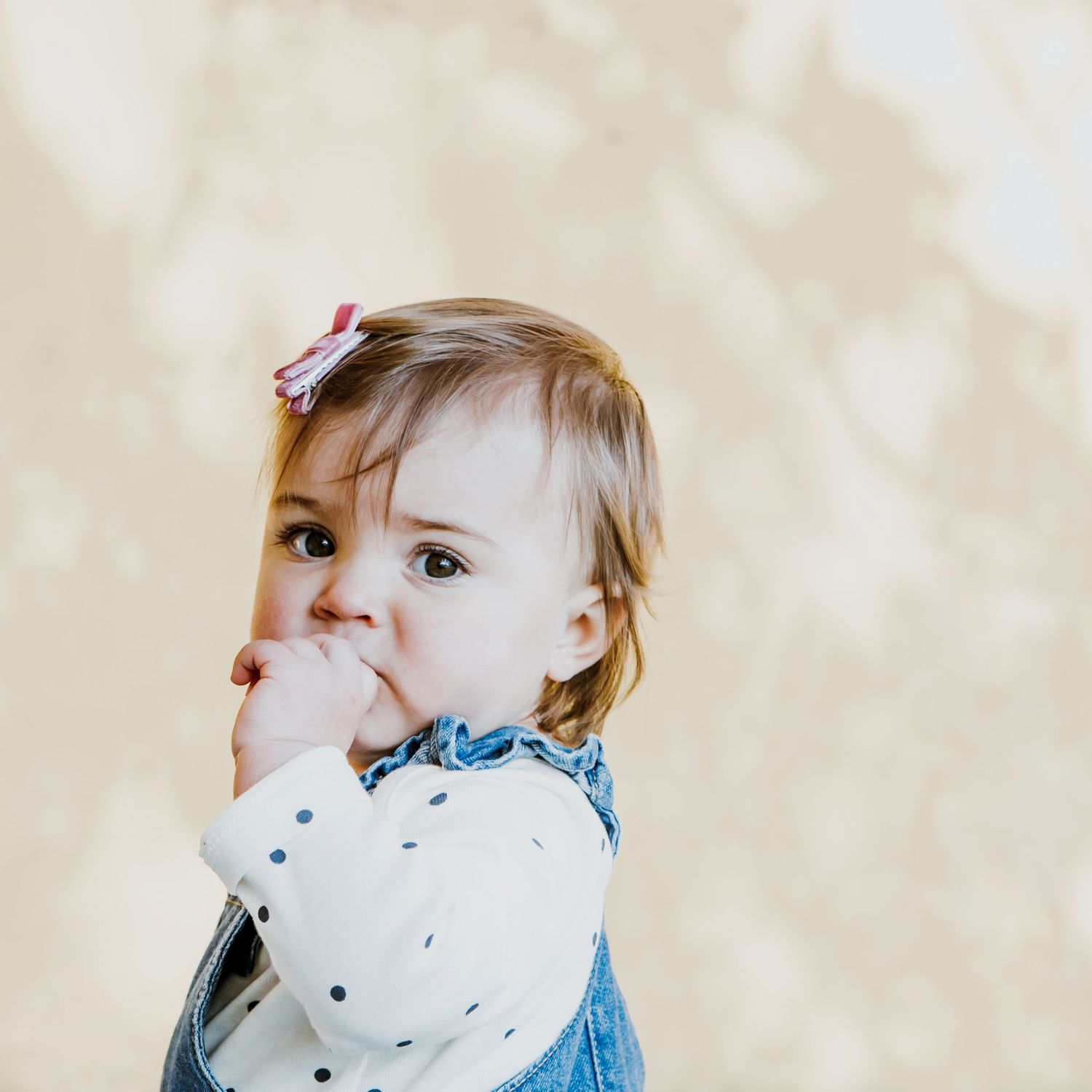 Portrait of a toddler girl looking towards the camera with her hand resting against her mouth during a natural children's photography sessio