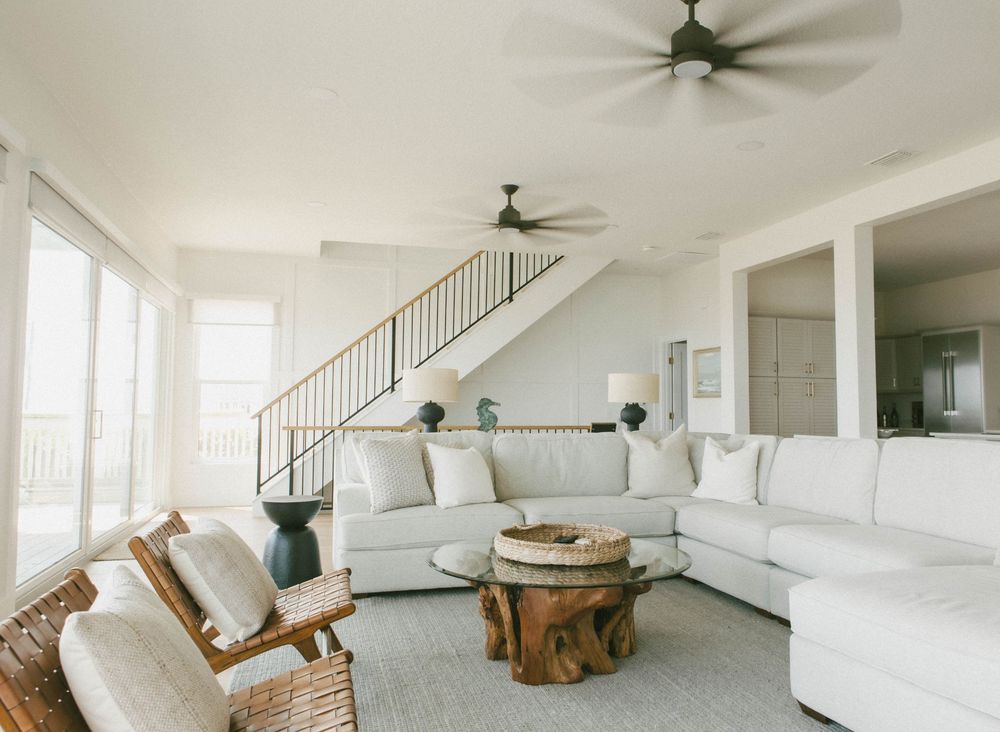 Bright coastal living room with white sectional sofa, natural wood coffee table and ceiling fans in airy space.