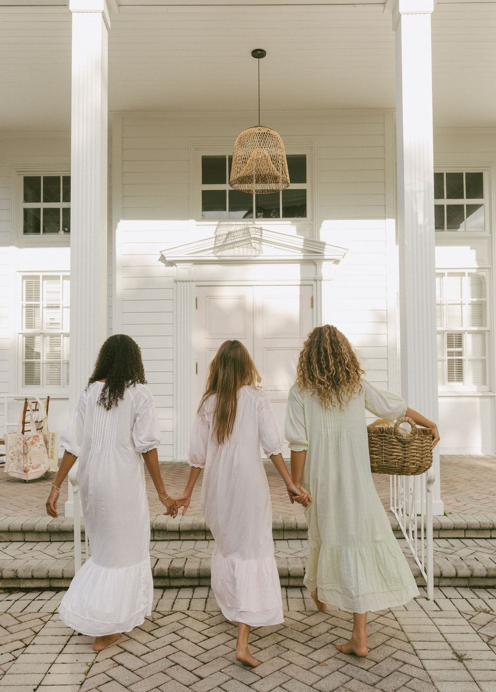 A row of people in white and light-colored dresses sitting on a white porch with columns in a vintage style setting.