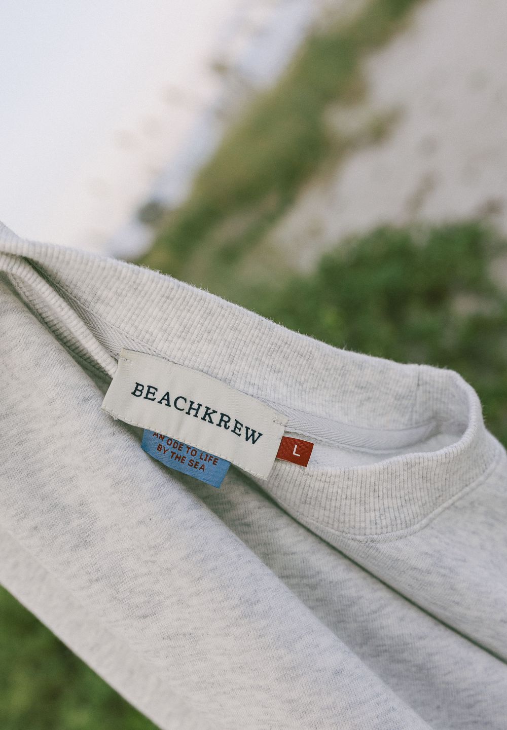 Product label detail showing 'BEACHKREW' text on a heather gray sweatshirt collar.