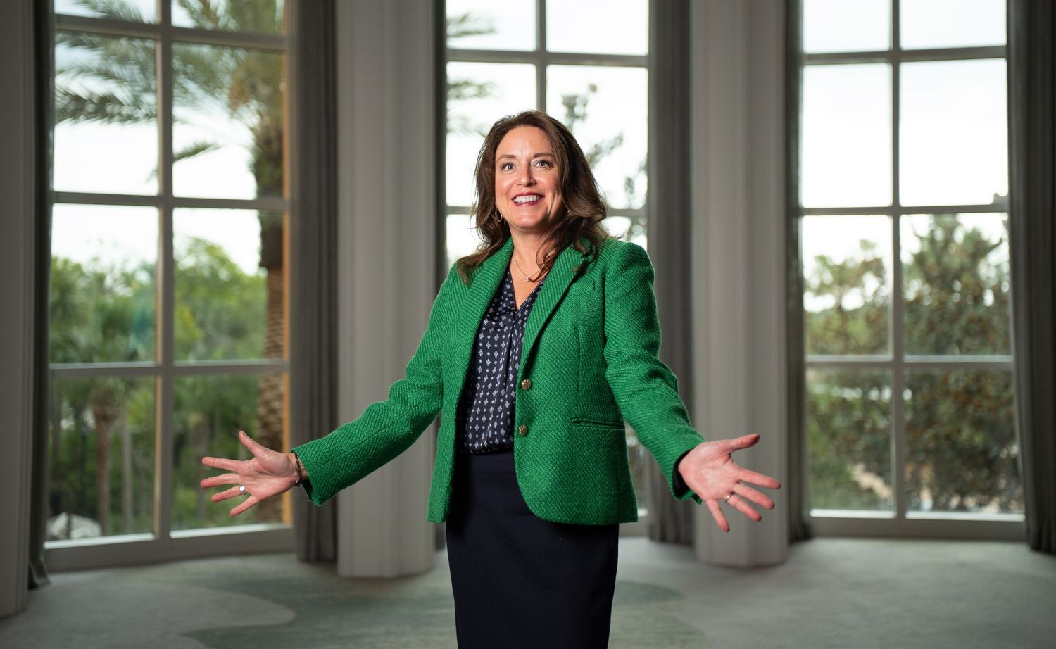 Professional woman in navy blazer and striped top smiling confidently against a light background.