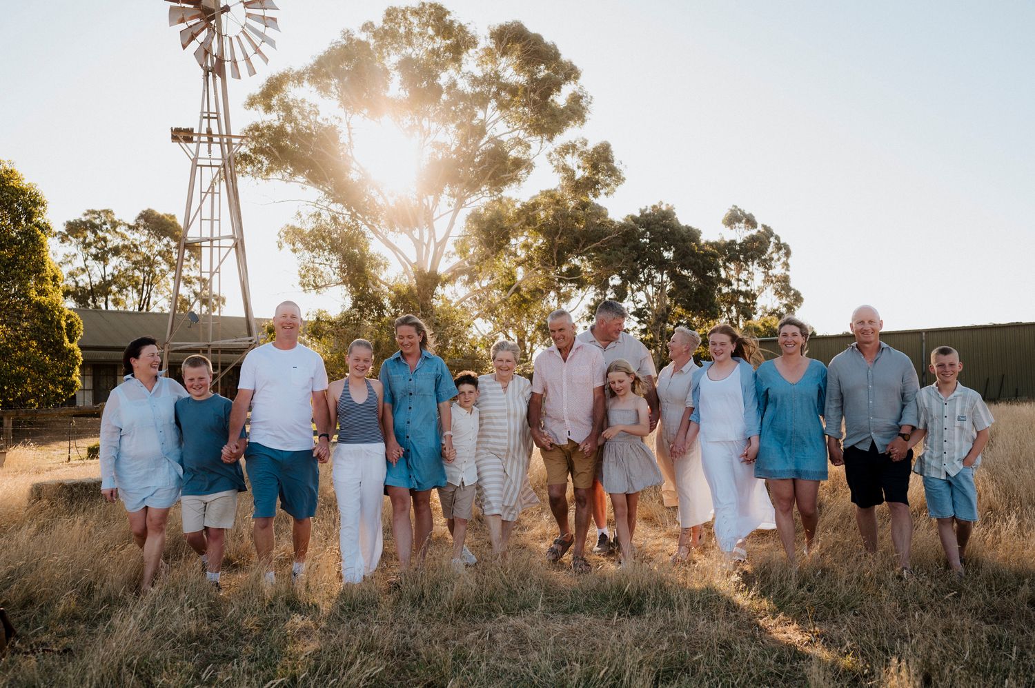 Large family group posing together in golden sunset light on a rural farm with windmill and eucalyptus trees.