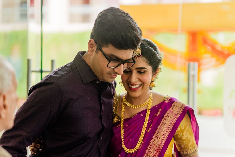 South Indian bride in purple silk saree with gold jewelry sharing joyful moment with groom.
