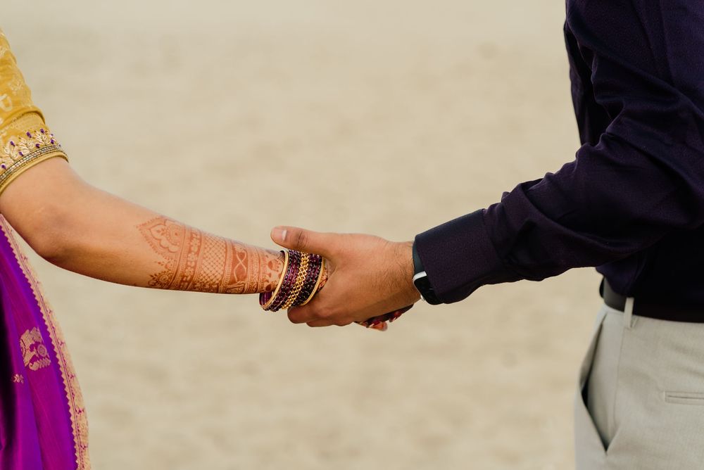Indian bride with henna and bangles holding groom's hand in traditional wedding ceremony.