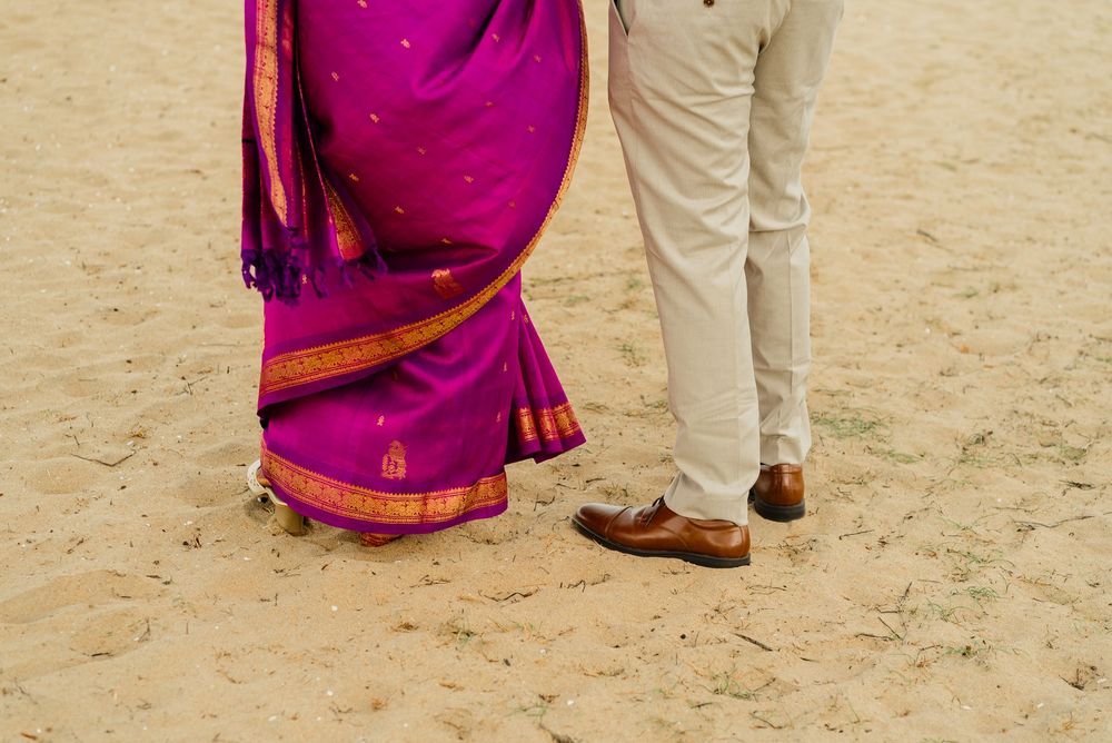 Couple in traditional Indian saree and beige trousers standing on sandy ground at an outdoor celebration.