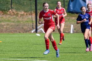Young female soccer player in red uniform sprinting on green turf during a youth girls soccer match.