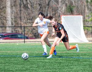 Two female soccer players compete for the ball on a green turf field during an outdoor youth soccer match.