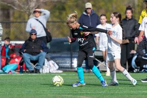 Young soccer players compete in a youth match, with a player in black dribbling against a white-uniformed opponent.