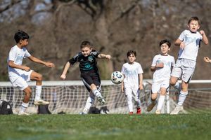 Young boys playing competitive soccer, with one player kicking the ball toward the goal during an outdoor match.