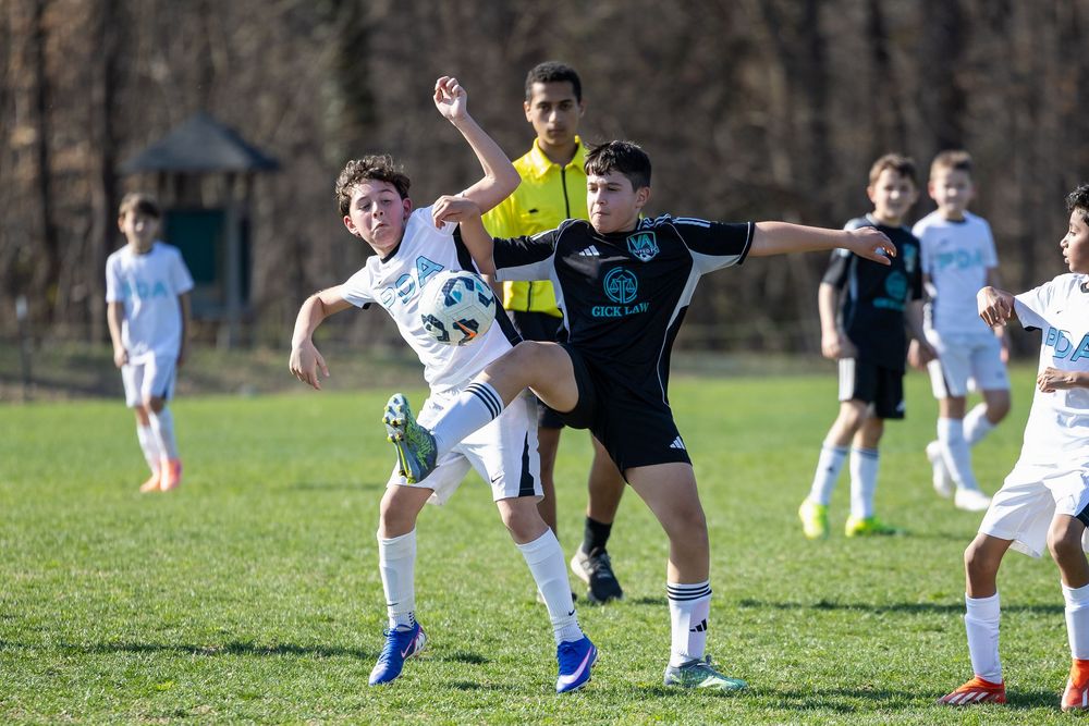 Two youth soccer players battle for the ball during an outdoor match on a green grass field.