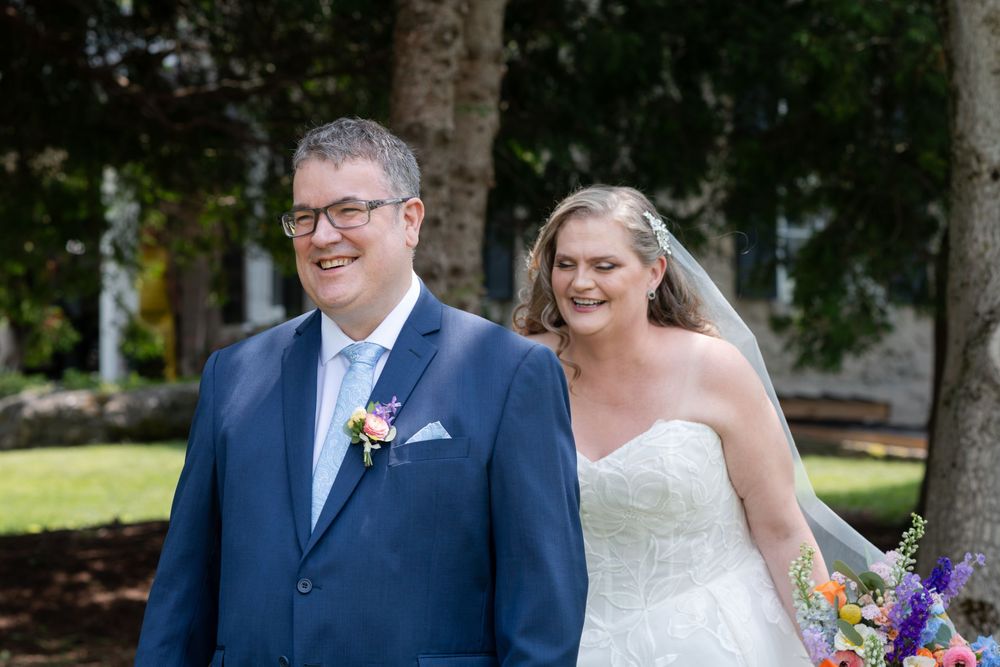 Bride and groom smiling outdoors on their wedding day, with colorful bouquet and blue suit in Guelph, Ontario.