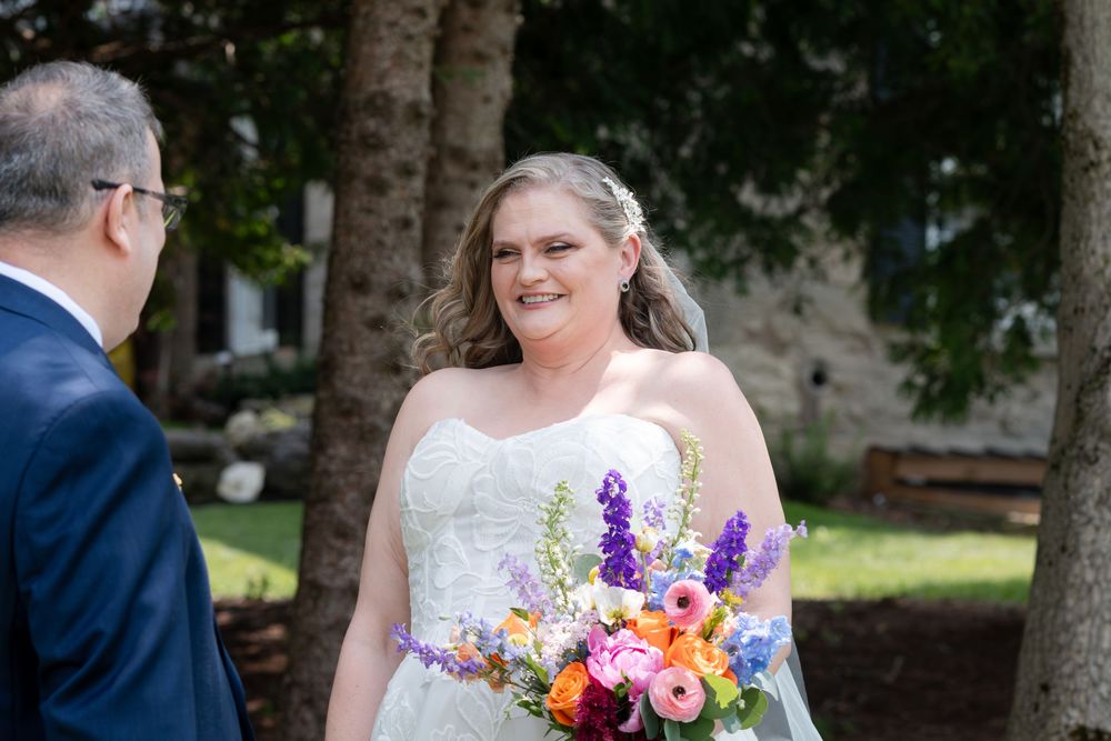 Smiling bride in strapless white gown holding colorful bouquet of purple, pink, and orange flowers outdoors in Guelph, Ontario.