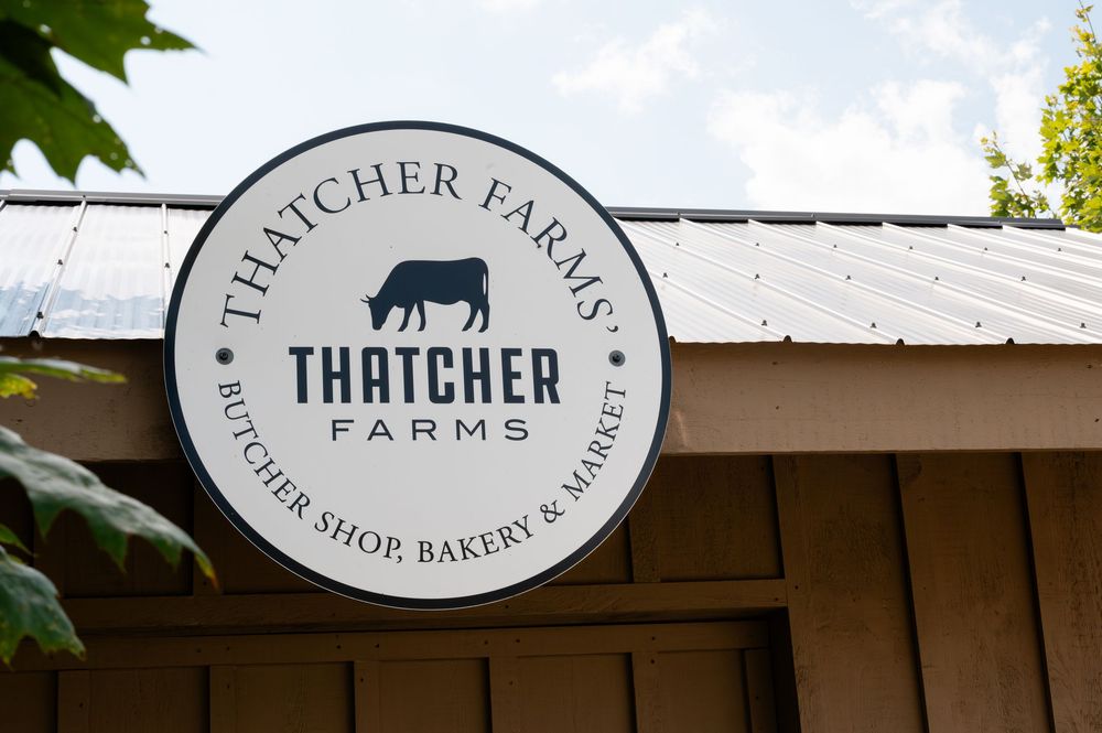 Thatcher Farms Butcher Shop, Bakery & Market round sign on a rustic wooden building exterior at barn swallow fields in guelph, ontario.