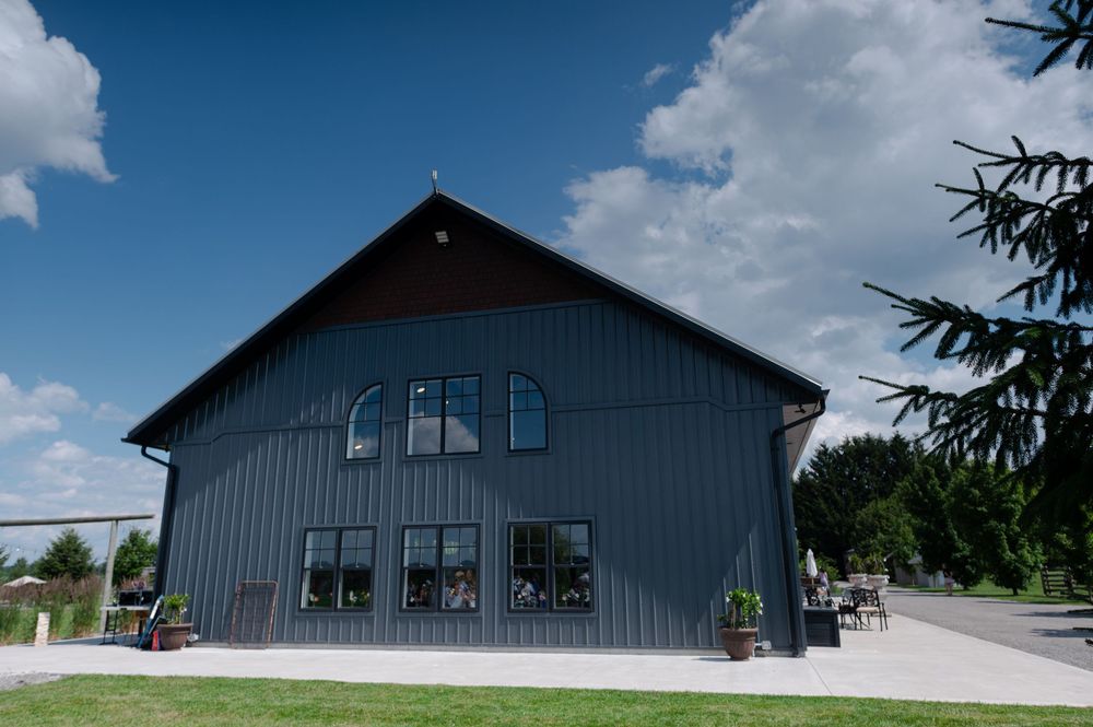 Dark gray barn-style building with large windows, surrounded by green lawn and trees at barn swallow fields in guelph, ontario.
