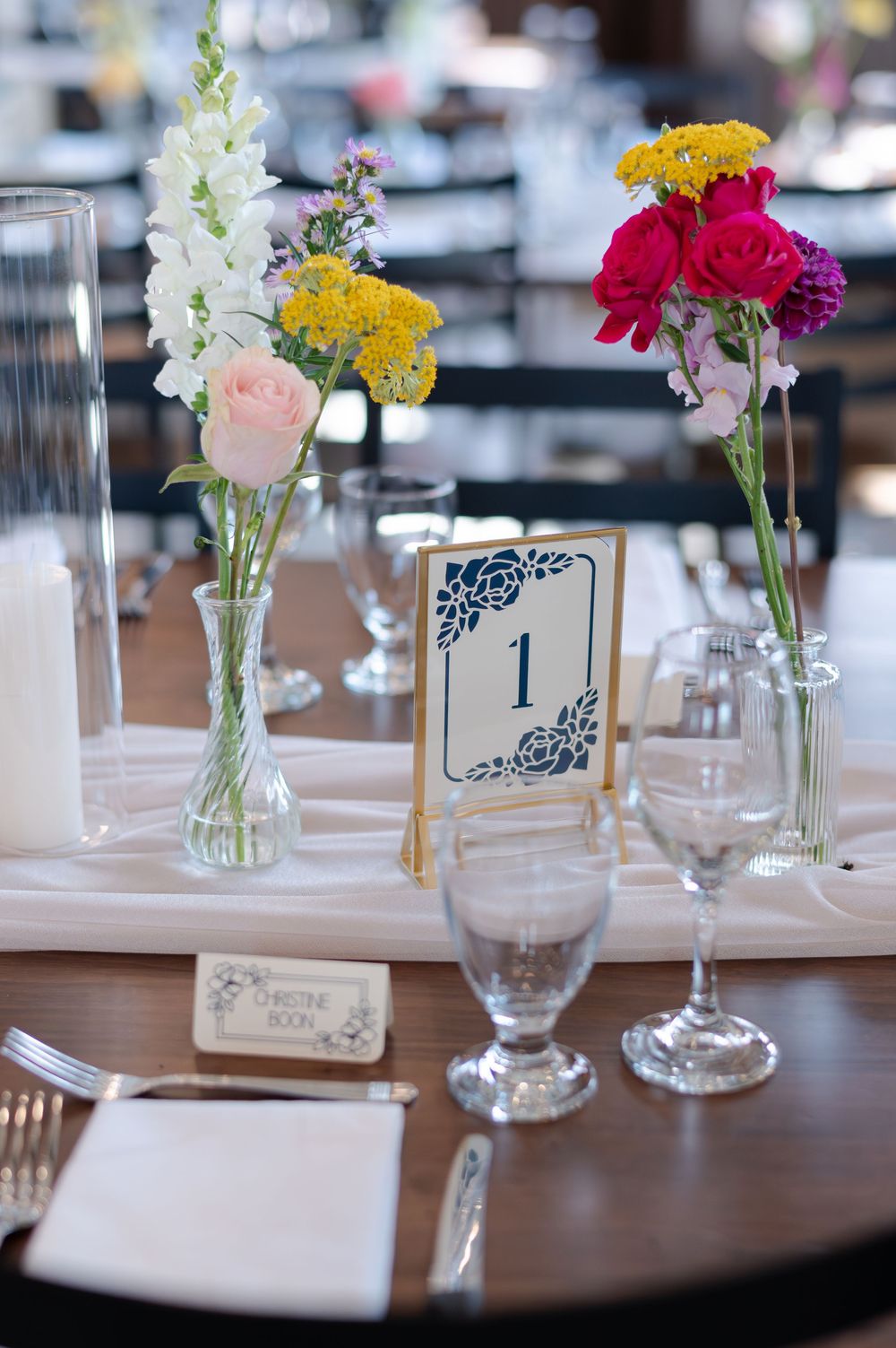 Wedding table centerpiece with colorful flowers in glass vases, place settings on white linen at barn swallow fields in guelph, ontario.