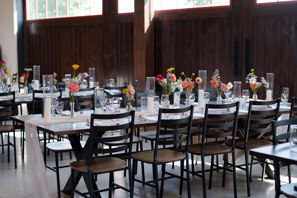 Elegant wedding reception hall with long tables, black chairs, and colorful floral centerpieces at barn swallow fields in guelph, ontario.