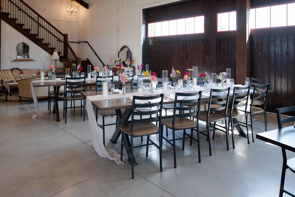 Elegant barn venue with long dining tables, black chairs, floral centerpieces, and rustic wooden doors at barn swallow fields in guelph