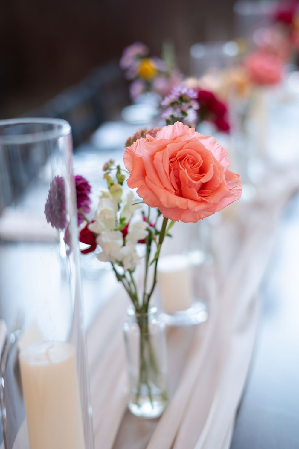 Coral rose in glass bud vase with candles on a blush table runner at a wedding reception at barn swallow fields in guelph, ontario.