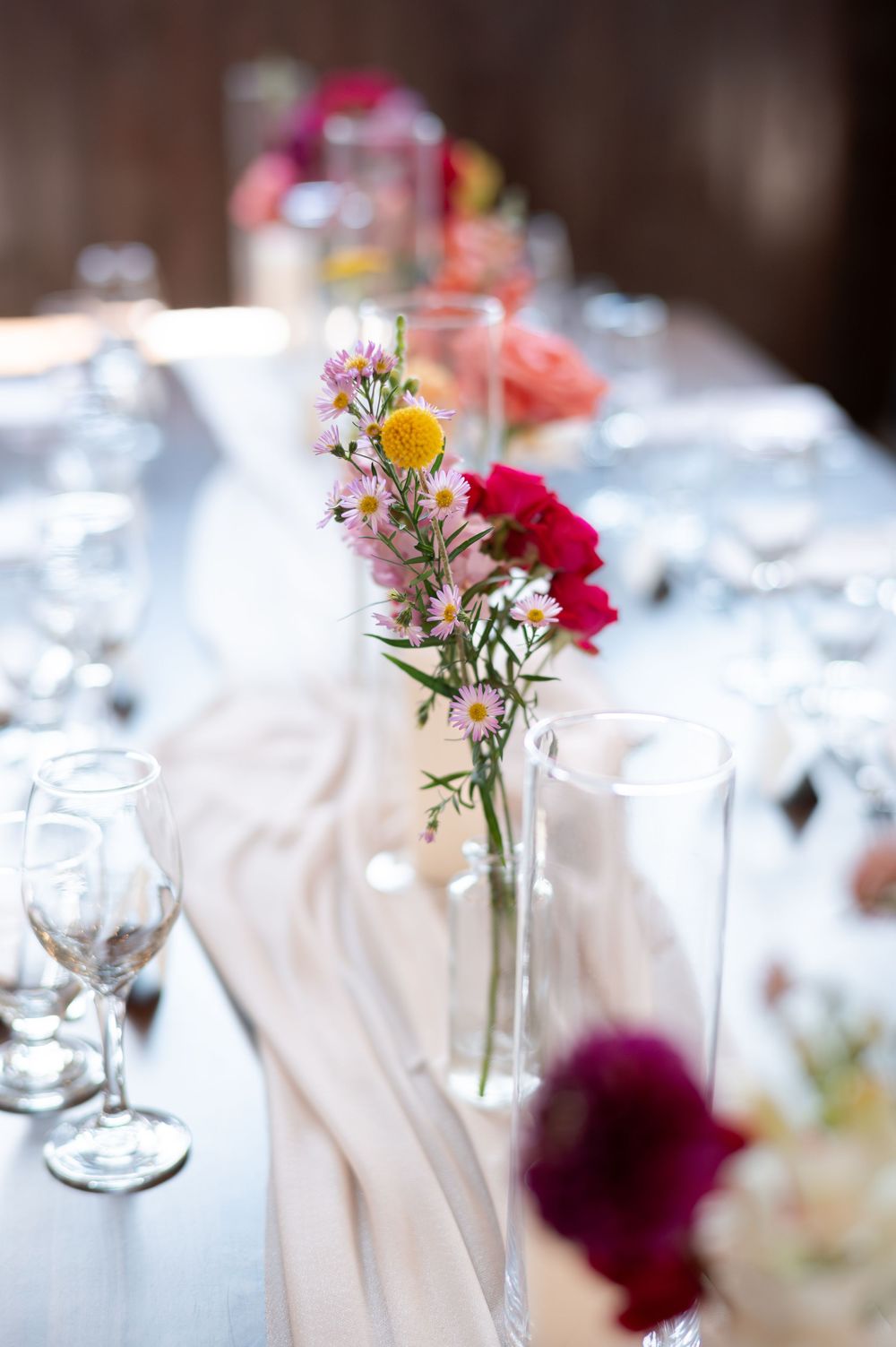 Elegant wedding table setting with colorful wildflowers in glass vases, and a soft blush table runner at barn swallow fields in guelph, ON