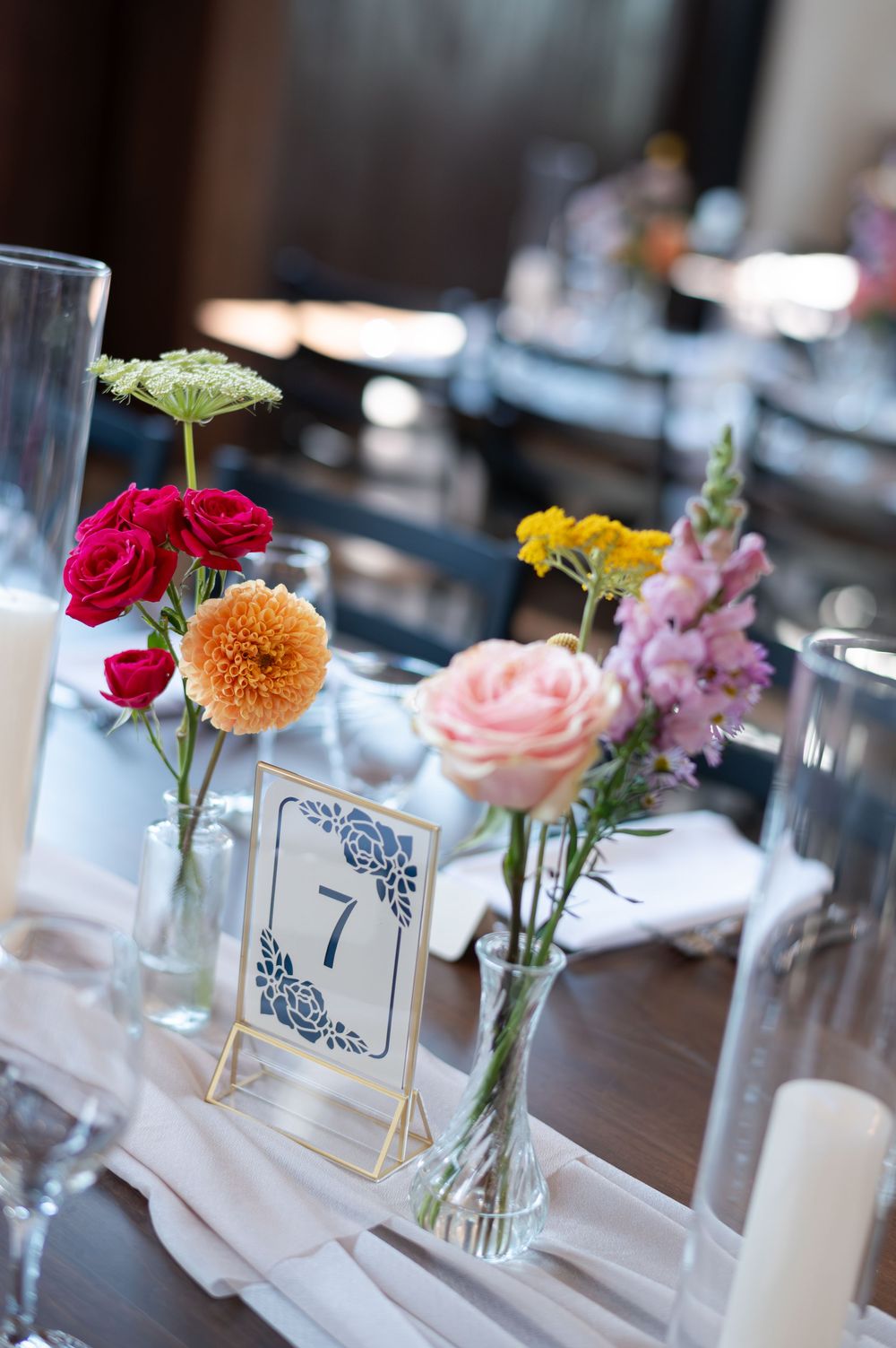 Colorful wedding table centerpiece with flowers in bud vases beside a navy table number at barn swallow fields in guelph, ontario.