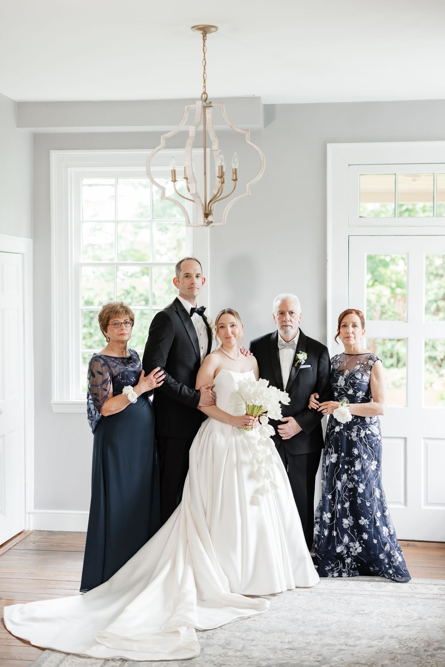 Formal wedding portrait of bride and groom with family members in navy formal wear inside elegant venue.