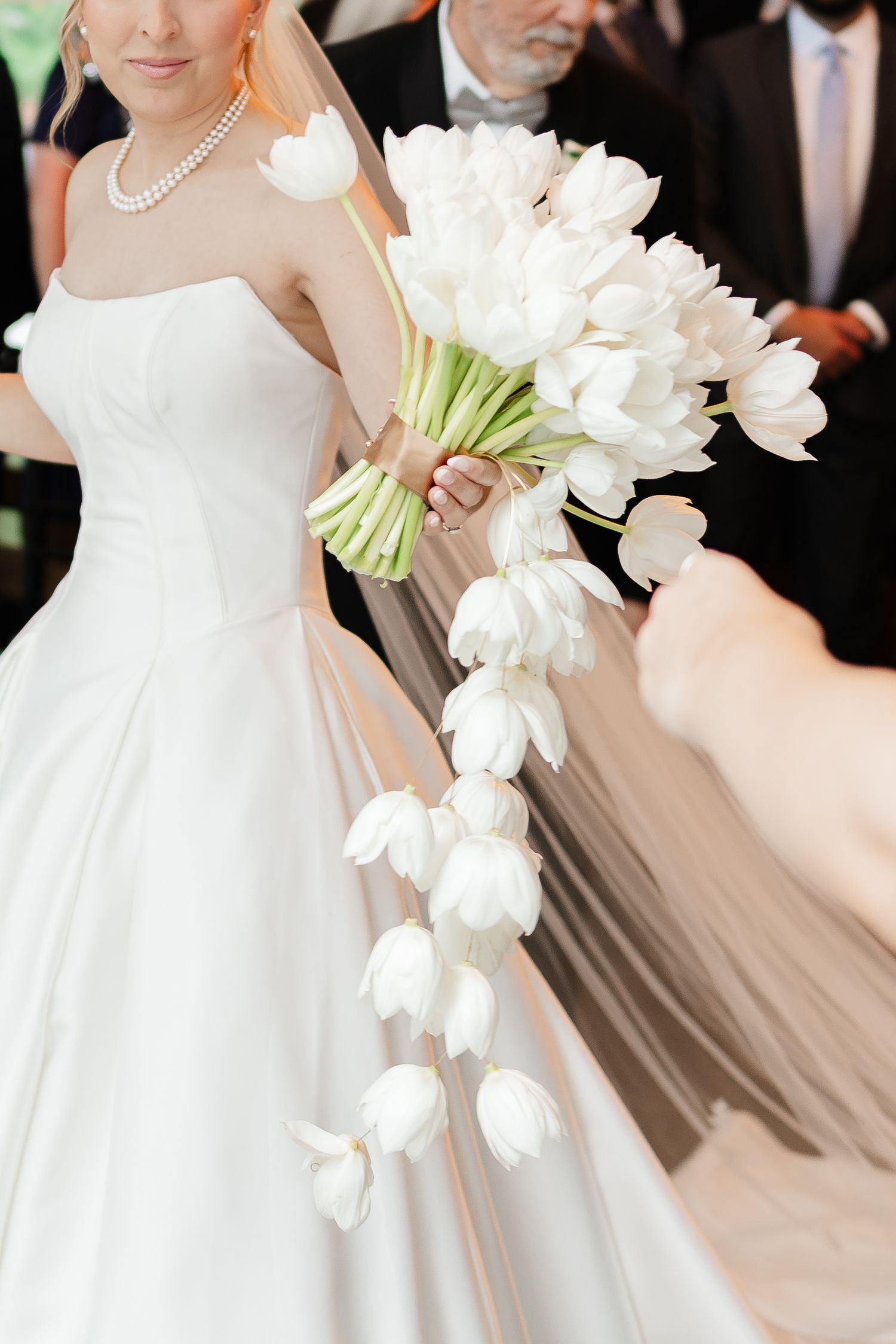 Bride in strapless white satin gown holds a cascading bouquet of white tulips at her wedding ceremony.