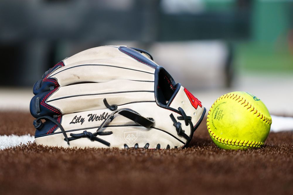 Softball glove personalized with name Lily Weebley beside a yellow softball on dirt field.
