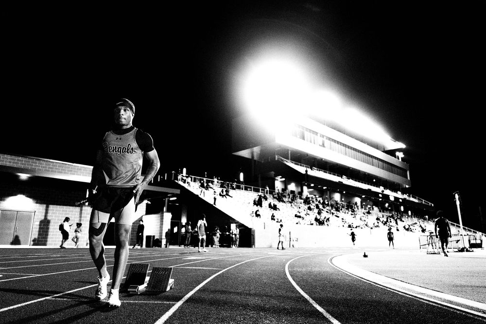 Black and white image of track athlete running under bright stadium lights at night.