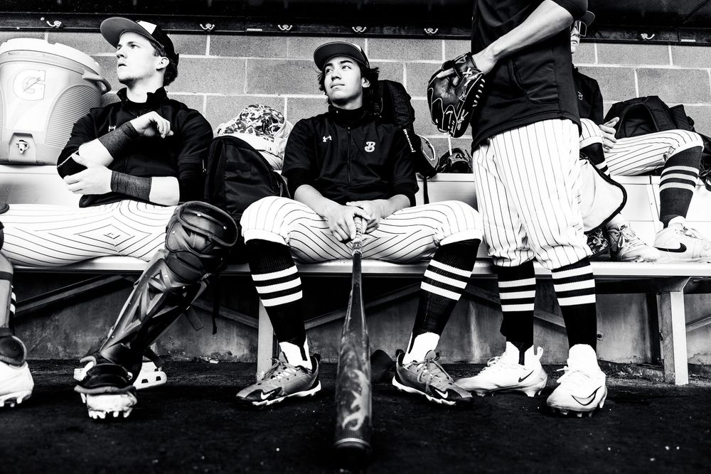 Black and white photo of baseball players resting on dugout bench during game.