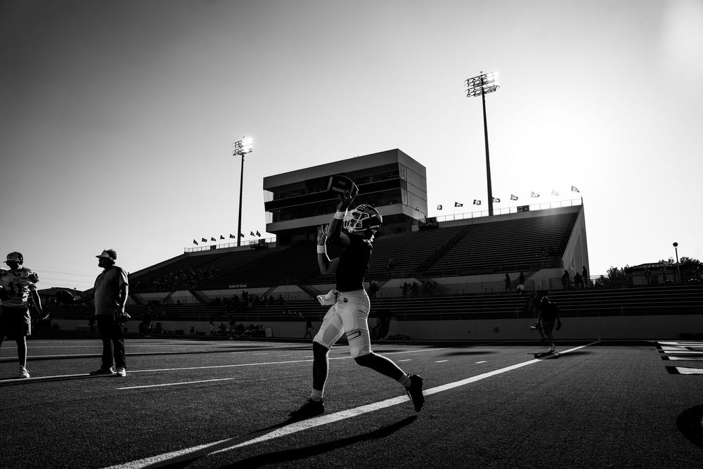 Black and white silhouette of football player warming up on field at dusk in stadium.