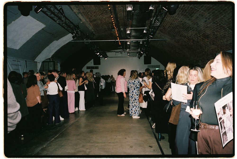 Guests mingle at an indoor event in a brick-vaulted venue with track lighting and artwork displays.