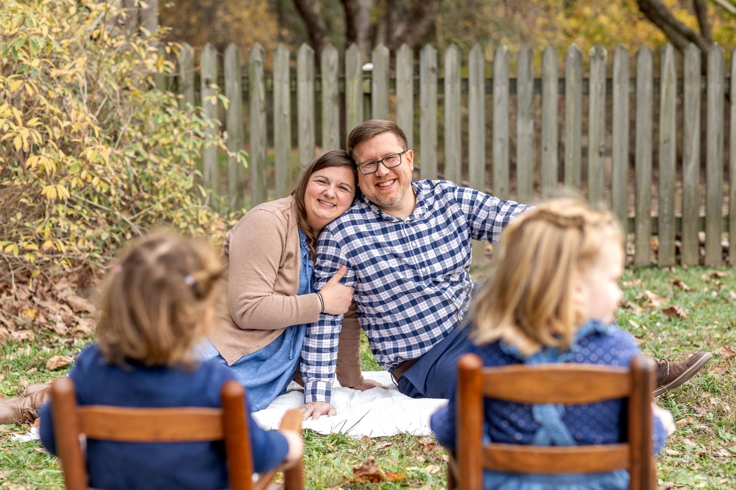 Casual outdoor family photography session with wooden fence and fall foliage.