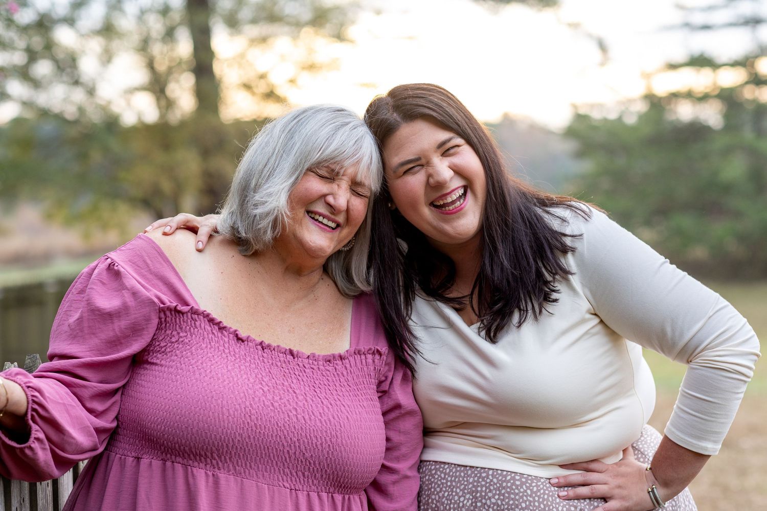 Two women in pink and white outfits share genuine laughter during outdoor photoshoot.