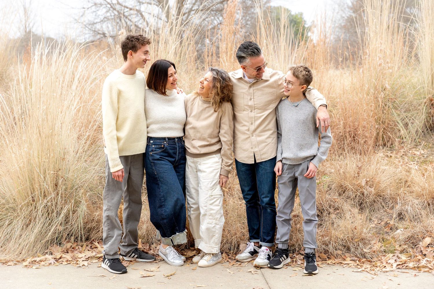 Family members in casual outfits sitting together on wooden steps during an outdoor autumn photoshoot.
