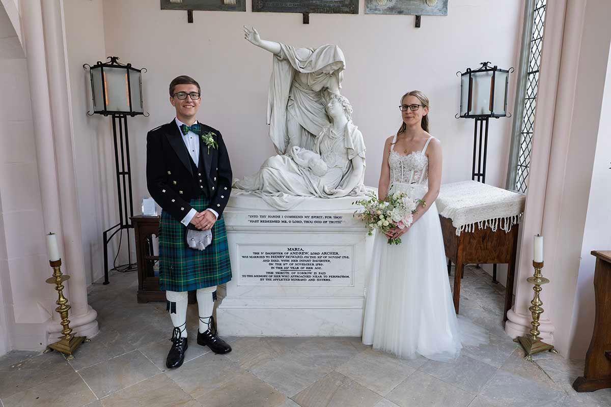 Bride and groom posing in a church beside a white marble statue on their wedding day.